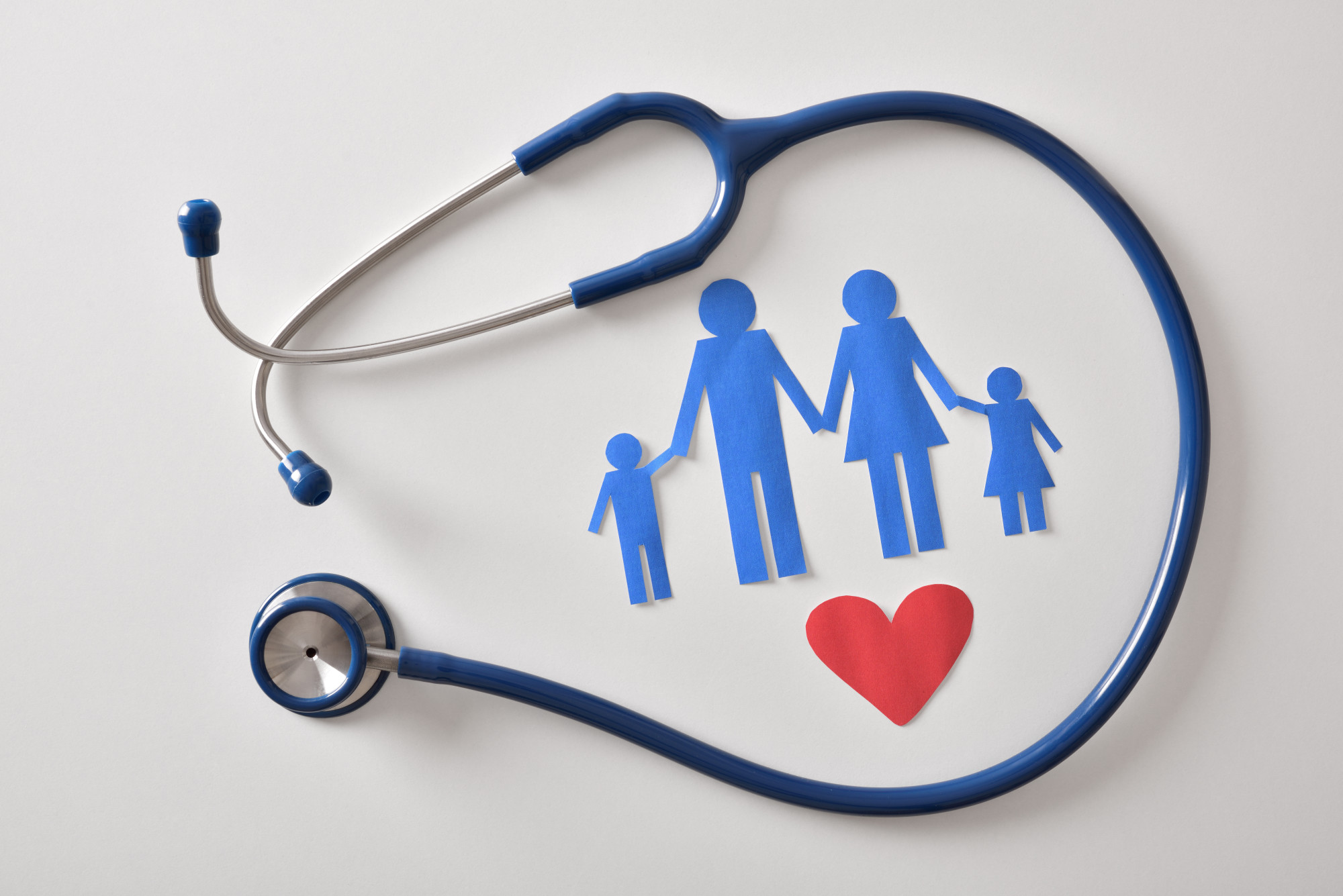 Concept of family medicine with ostetoscope and paper cut of family and heart on a white table. Top view. Horizontal composition.